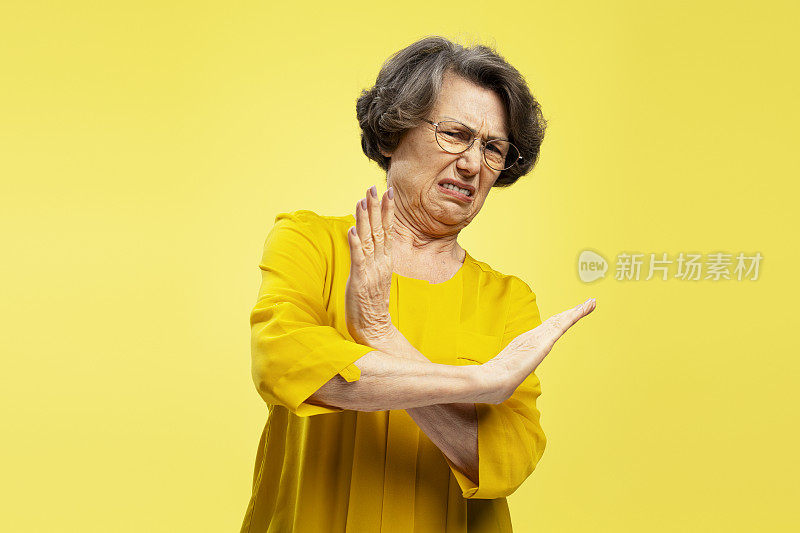 Portrait of unhappy, gray haired woman showing hands stop gesture isolated on yellow background